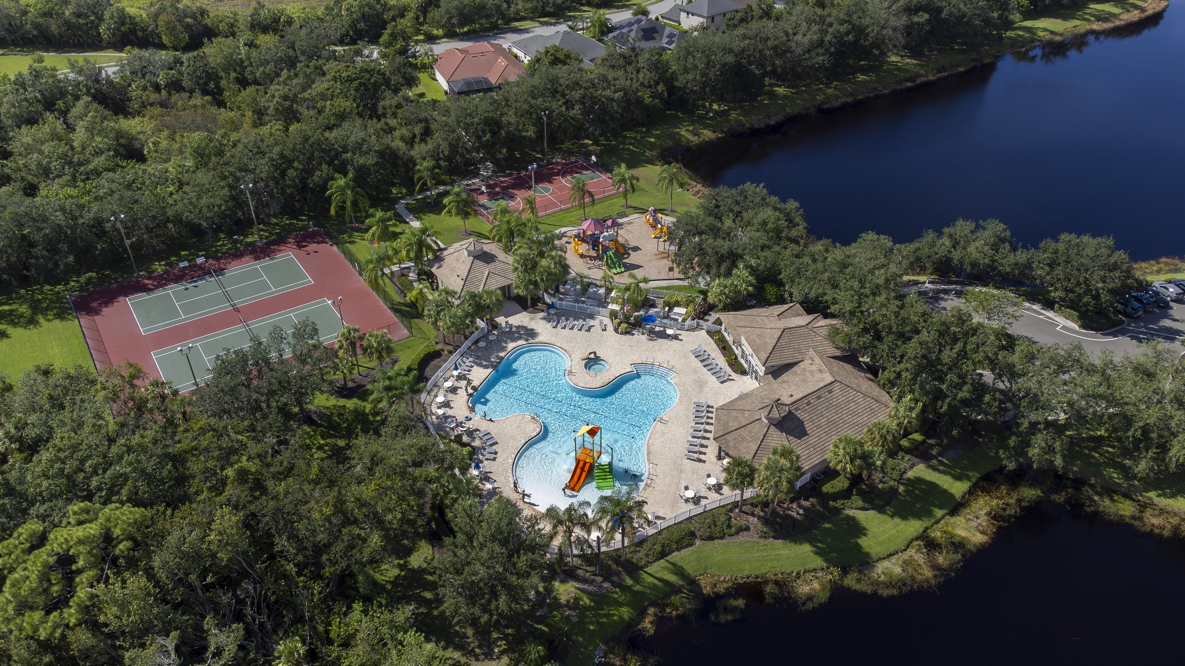 Resort-style lakeside community pool, splash pad, and tennis courts — Sarasota drone aerial