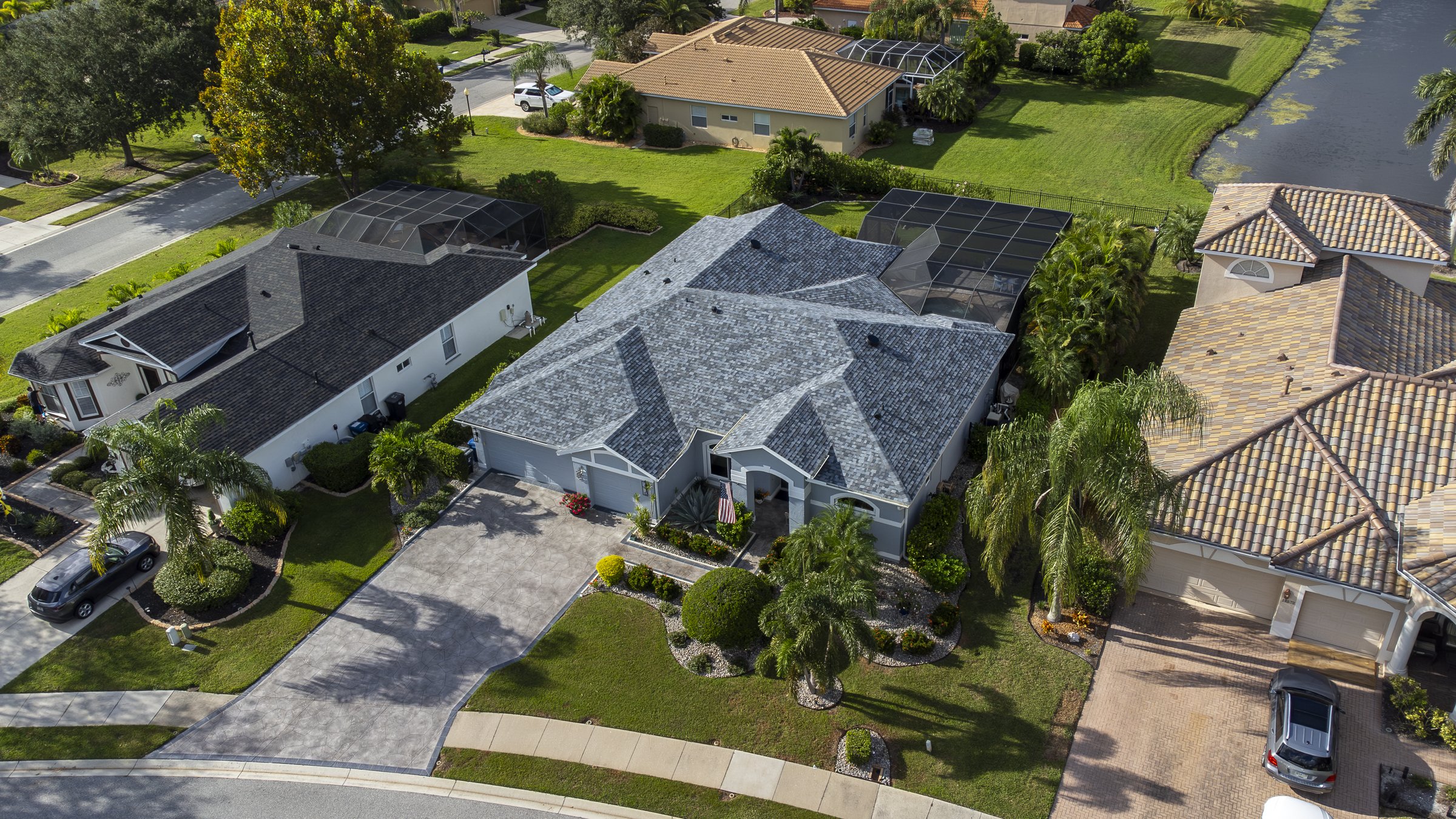 Angled drone aerial of a Sarasota luxury home with grey roof and paver driveway
