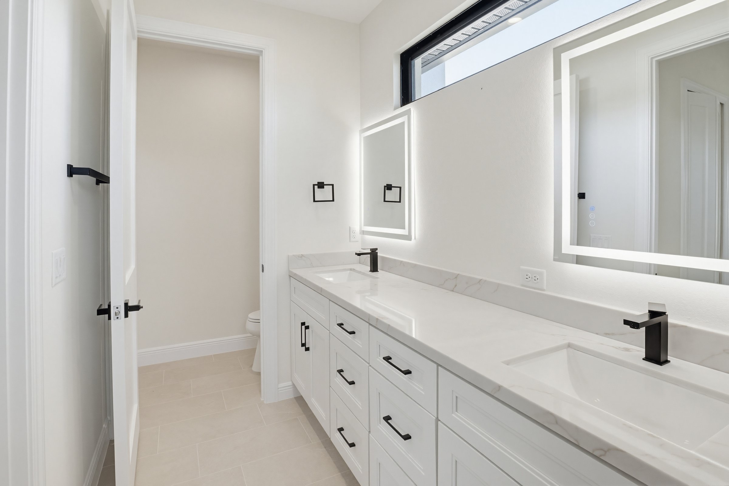 Modern primary bathroom with backlit mirrors and marble vanity in a Sarasota home